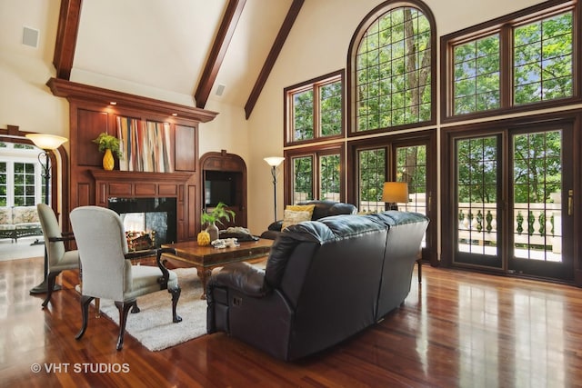 living room with a high end fireplace, a towering ceiling, a healthy amount of sunlight, and dark hardwood / wood-style floors