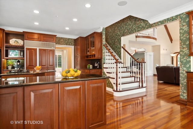 kitchen with dark stone countertops, paneled built in fridge, crown molding, and light wood-type flooring