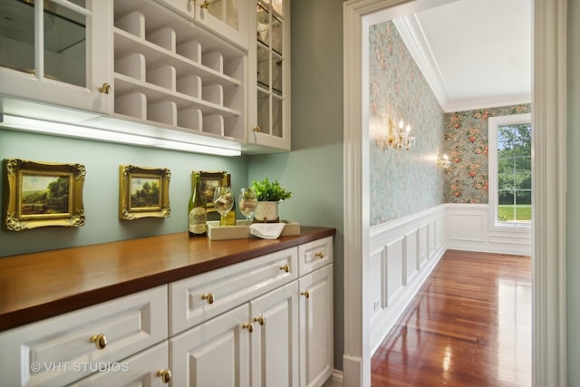 bar with hardwood / wood-style floors, butcher block countertops, ornamental molding, and white cabinetry