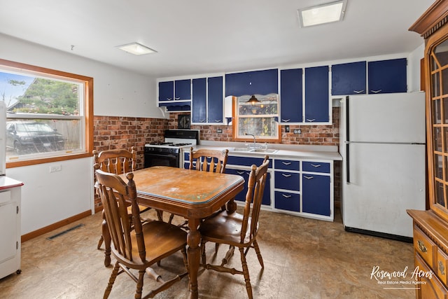 kitchen with sink, white appliances, blue cabinetry, and brick wall