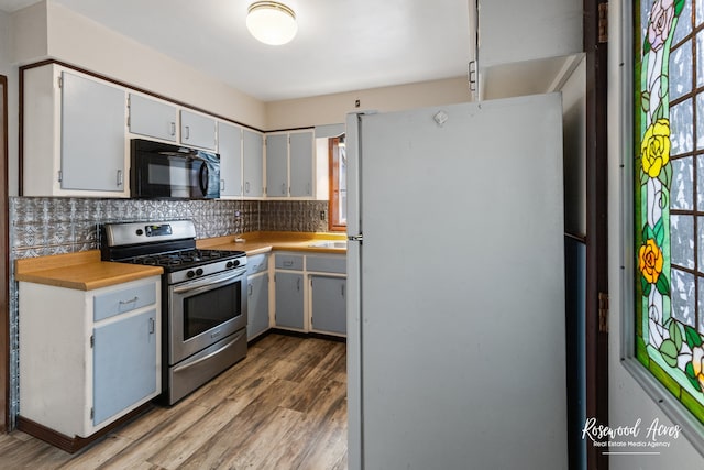 kitchen with wood-type flooring, white fridge, a healthy amount of sunlight, and stainless steel gas range