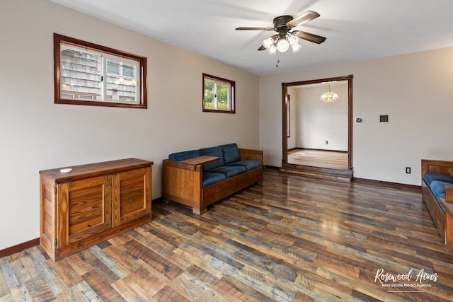 sitting room with ceiling fan with notable chandelier and dark wood-type flooring