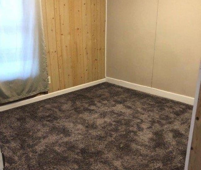 unfurnished room with baseboards, wood walls, and dark carpet