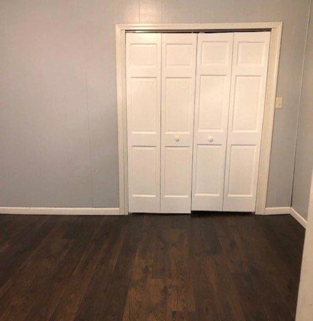 unfurnished bedroom featuring a closet, dark wood-type flooring, and baseboards