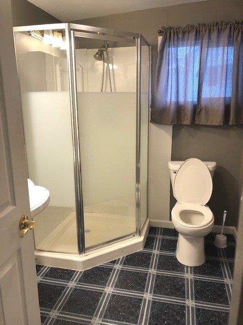 bathroom featuring toilet, baseboards, and a stall shower