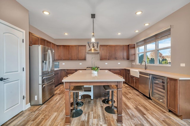 kitchen with appliances with stainless steel finishes, light wood-type flooring, sink, wine cooler, and hanging light fixtures