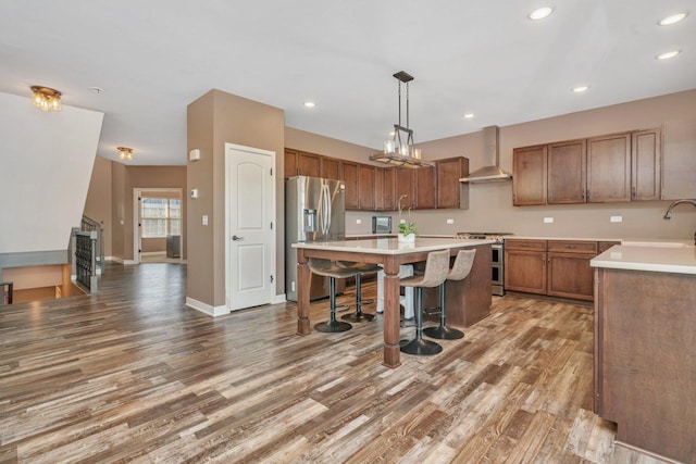 kitchen with wall chimney range hood, a kitchen breakfast bar, decorative light fixtures, appliances with stainless steel finishes, and hardwood / wood-style flooring