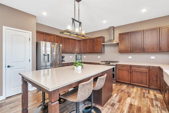 kitchen featuring stainless steel appliances, wall chimney range hood, a kitchen breakfast bar, pendant lighting, and light hardwood / wood-style floors