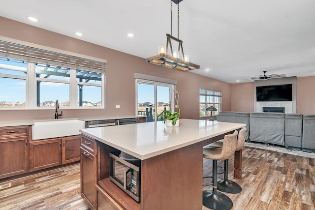 kitchen with ceiling fan, sink, a center island, hanging light fixtures, and light hardwood / wood-style floors