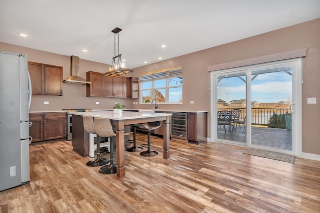 kitchen featuring a kitchen island, wall chimney range hood, white fridge, stainless steel stove, and wine cooler