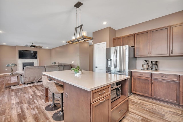 kitchen with ceiling fan, a tile fireplace, pendant lighting, a center island, and light hardwood / wood-style floors