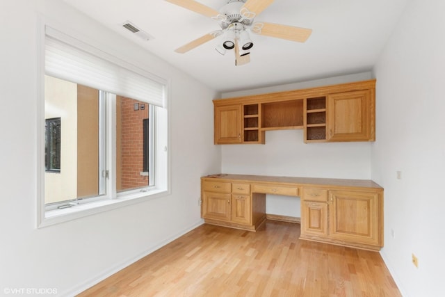 unfurnished office featuring built in desk, light hardwood / wood-style flooring, and ceiling fan