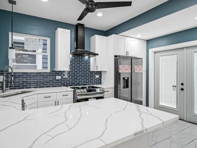 kitchen featuring light stone countertops, stainless steel appliances, sink, wall chimney range hood, and decorative light fixtures