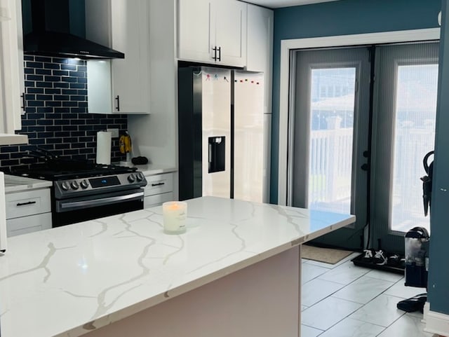 kitchen featuring white cabinetry, light stone countertops, wall chimney range hood, decorative backsplash, and appliances with stainless steel finishes