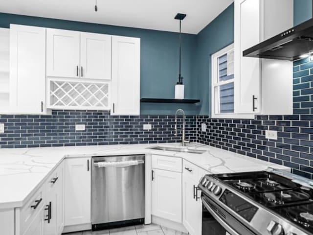 kitchen featuring sink, wall chimney exhaust hood, stainless steel appliances, decorative light fixtures, and white cabinets