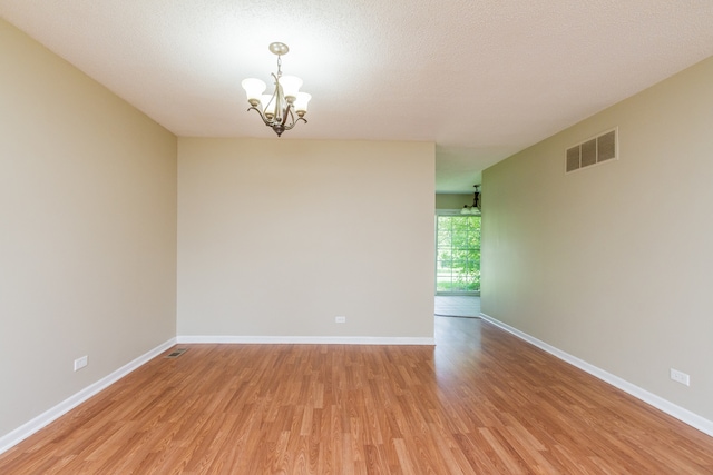 unfurnished room featuring a notable chandelier, a textured ceiling, and light hardwood / wood-style flooring