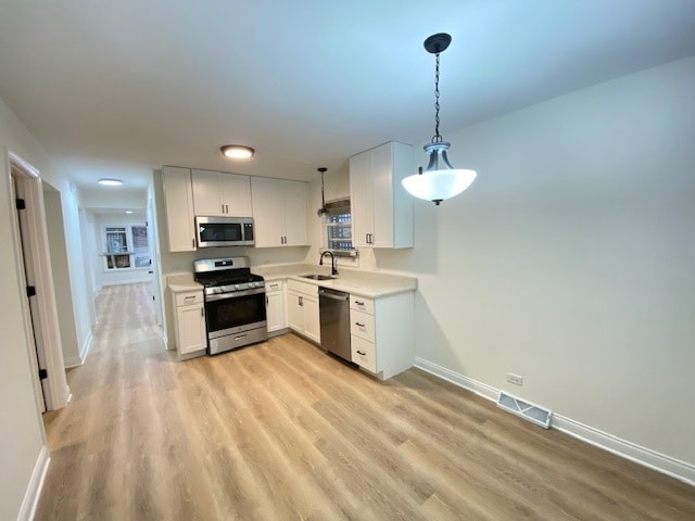 kitchen featuring sink, hanging light fixtures, light hardwood / wood-style floors, white cabinets, and appliances with stainless steel finishes