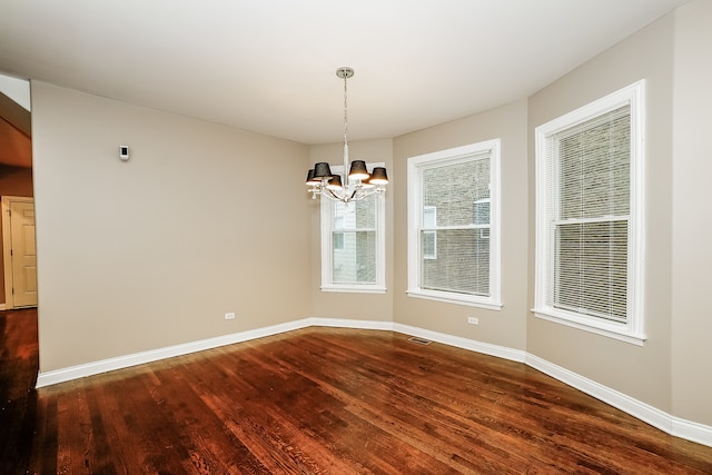 spare room with dark hardwood / wood-style floors and an inviting chandelier