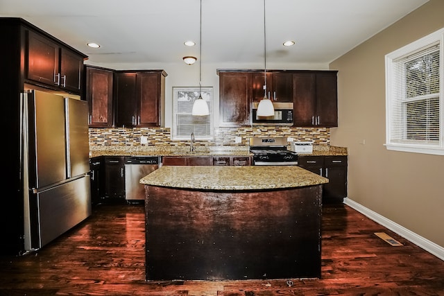 kitchen featuring pendant lighting, light stone countertops, a kitchen island, dark hardwood / wood-style flooring, and stainless steel appliances