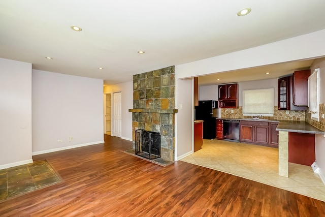 kitchen with decorative backsplash, light wood-type flooring, a large fireplace, sink, and black appliances