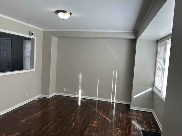 empty room featuring baseboards, visible vents, dark wood finished floors, and ornamental molding