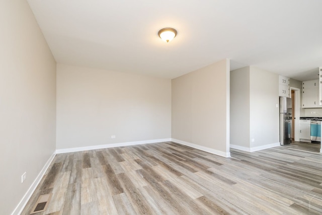 empty room with light wood-style floors, visible vents, and baseboards