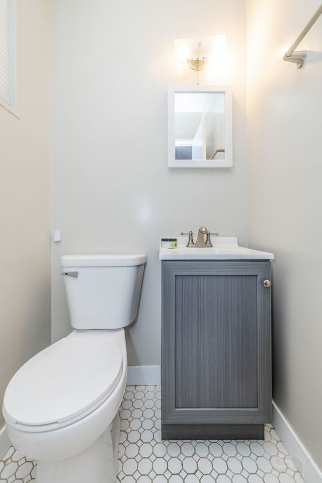 half bathroom featuring toilet, baseboards, and vanity