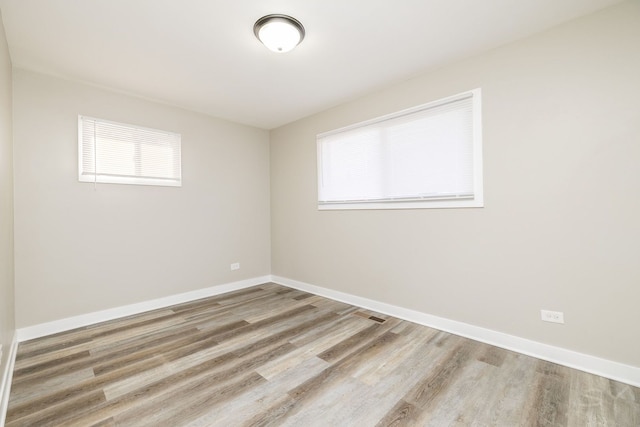 unfurnished room featuring wood finished floors, a wealth of natural light, and baseboards