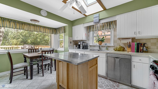 kitchen with a skylight, sink, stainless steel dishwasher, decorative backsplash, and white cabinets