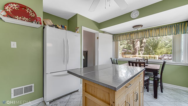 kitchen featuring ceiling fan, light brown cabinets, light tile patterned flooring, white refrigerator, and a kitchen island