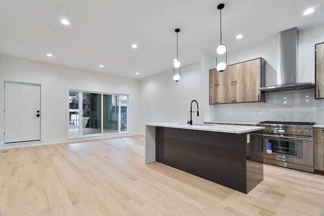 kitchen with wall chimney exhaust hood, light stone countertops, an island with sink, stainless steel range, and decorative light fixtures