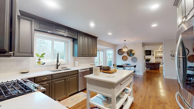 kitchen featuring appliances with stainless steel finishes, tasteful backsplash, sink, hanging light fixtures, and light hardwood / wood-style floors