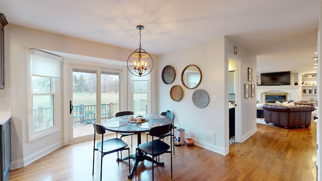 dining area featuring a notable chandelier, a brick fireplace, and light hardwood / wood-style flooring