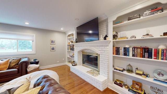 living room with built in shelves, a fireplace, and light wood-type flooring