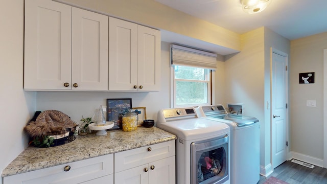 clothes washing area featuring cabinets, dark wood-type flooring, and washing machine and clothes dryer