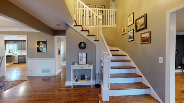 staircase with crown molding, sink, and hardwood / wood-style floors