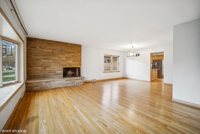 unfurnished living room featuring a fireplace, a chandelier, and light wood-type flooring