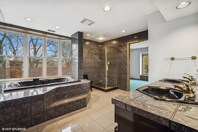 bathroom with tiled bath, a wealth of natural light, tile patterned flooring, and dual sinks