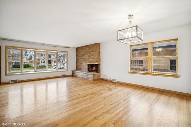 unfurnished living room with a stone fireplace, hardwood / wood-style floors, and an inviting chandelier