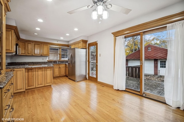 kitchen with appliances with stainless steel finishes, light wood-type flooring, ceiling fan, sink, and dark stone countertops