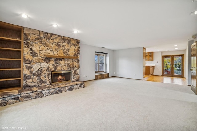 unfurnished living room featuring a fireplace, french doors, and light colored carpet