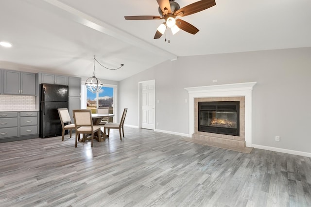 dining space with a tile fireplace, lofted ceiling with beams, light hardwood / wood-style floors, and ceiling fan with notable chandelier