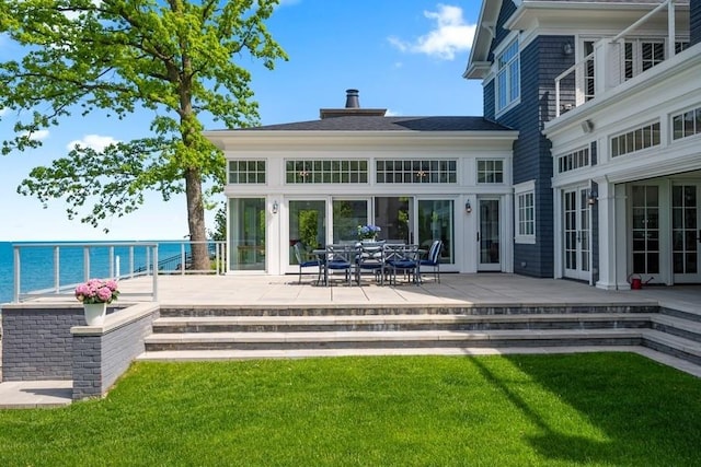 back of house with a patio area, a lawn, and a water view