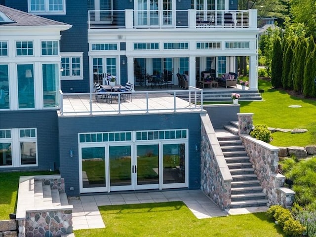 rear view of property featuring a balcony, a yard, french doors, and a patio