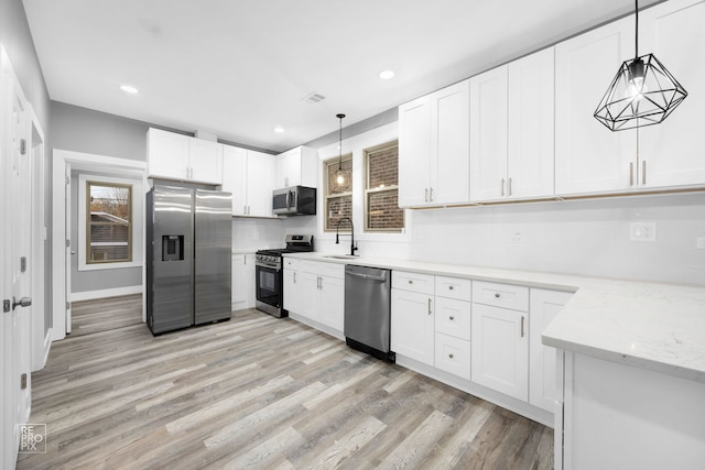 kitchen with appliances with stainless steel finishes, decorative light fixtures, white cabinetry, and sink