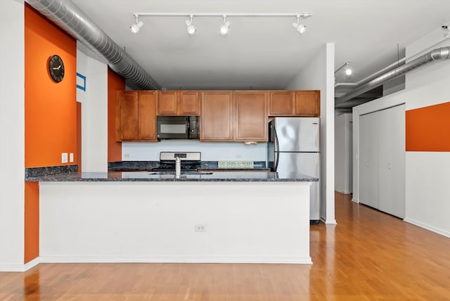 kitchen featuring kitchen peninsula, dark stone countertops, stainless steel appliances, and light wood-type flooring