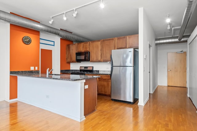 kitchen with sink, stainless steel appliances, kitchen peninsula, dark stone countertops, and light hardwood / wood-style floors