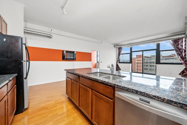 kitchen featuring dark stone counters, black fridge, sink, stainless steel dishwasher, and light hardwood / wood-style floors