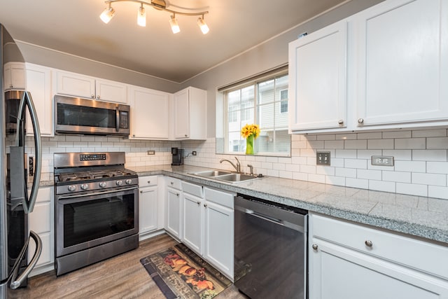 kitchen with light wood-type flooring, backsplash, stainless steel appliances, sink, and white cabinets