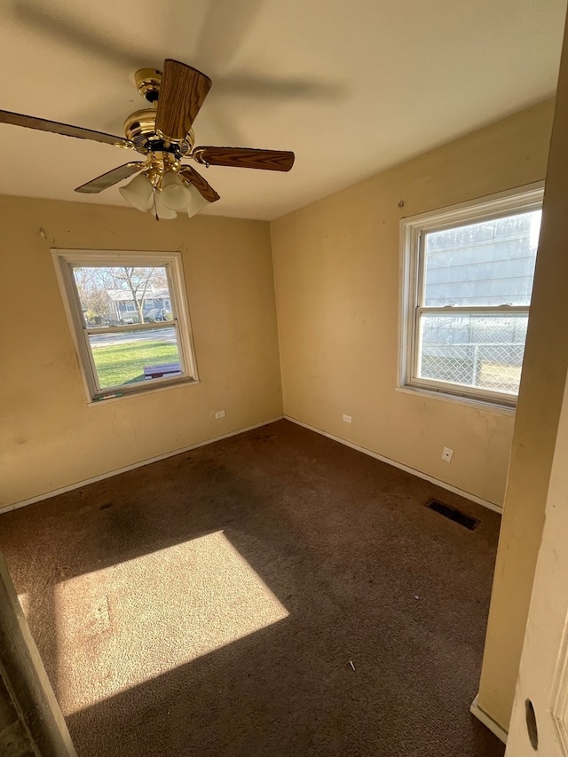 unfurnished room featuring ceiling fan, a healthy amount of sunlight, and dark carpet